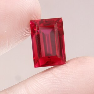 Puede incluir: Una piedra preciosa rectangular de color rojo intenso con un corte facetado.