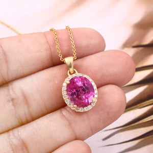 May include: A gold chain necklace with a pink oval gemstone pendant surrounded by a halo of smaller clear gemstones.