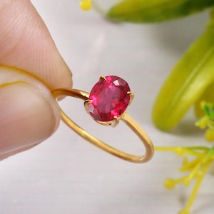 Op de afbeelding: Een gouden ring met een helderrode ovale edelsteen. De ring is simpel en elegant.