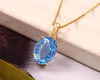 Puede incluir: Un collar de cadena de oro con un colgante de topacio ovalado azul claro.