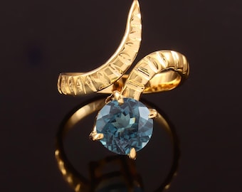 Könnte beinhalten: Ein goldener Ring mit einem blauen Edelstein, der in einem strukturierten, gebogenen Band gefasst ist.