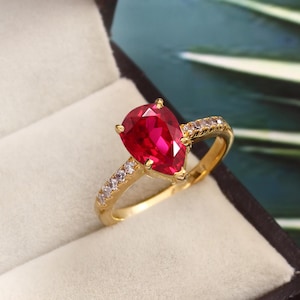 Könnte beinhalten: Ein goldener Ring mit einem birnenförmigen Rubin-Edelstein und einer Reihe kleiner, klarer Steine.