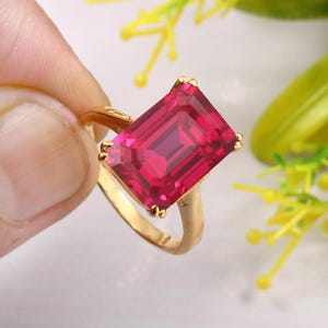 Puede incluir: Un anillo de oro con una gran piedra preciosa rosa brillante de talla esmeralda.