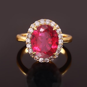 May include: A gold ring with a large oval-shaped ruby surrounded by a halo of smaller diamonds.