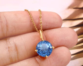 Puede incluir: Un collar de cadena de oro con un colgante redondo de piedra azul.