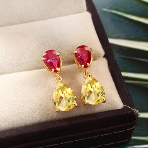 May include: A pair of gold earrings with teardrop-shaped red and yellow gemstones. The earrings are in a jewelry box.