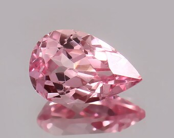 May include: A pear-shaped pink gemstone with a faceted cut. The gemstone is set against a white background.
