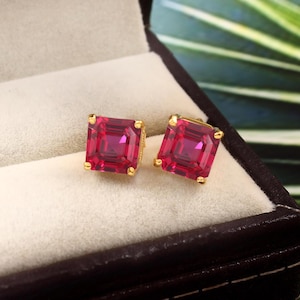 May include: A pair of gold earrings with square-shaped red gemstones.