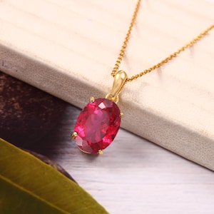 May include: A gold chain necklace with a large, oval-shaped, red gemstone pendant.
