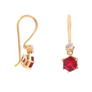 Puede incluir: Un par de pendientes de oro con una piedra preciosa roja y una pequeña piedra preciosa transparente. Los pendientes tienen un diseño de gota y están hechos de oro.
