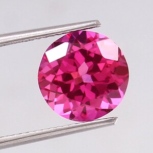 Puede incluir: Una gema rosa vibrante con un corte redondo y una superficie facetada.