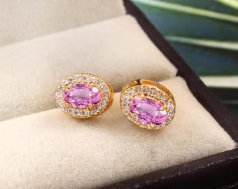 May include: A pair of gold earrings with oval-shaped pink gemstones surrounded by a halo of smaller clear gemstones.