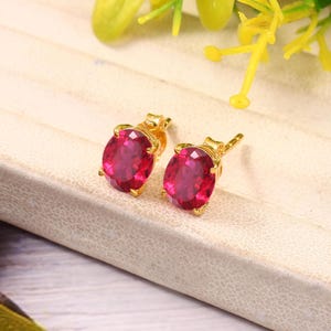 Puede incluir: Un par de pendientes de oro con piedras preciosas rojas de forma ovalada.