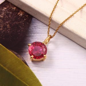 May include: A gold chain necklace with a round red gemstone pendant.