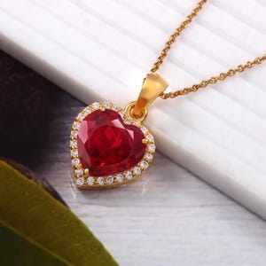 May include: A gold heart-shaped pendant necklace with a large red gemstone surrounded by smaller clear gemstones.