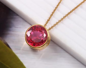 Puede incluir: Un collar de cadena de oro con un colgante redondo que presenta una gran piedra preciosa roja brillante.