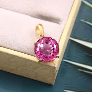 May include: A gold pendant featuring a large, round, pink gemstone set in a gold bezel setting.