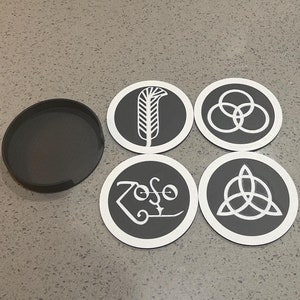 May include: Four round black coasters with white designs. The designs include a feather, a circle with three rings, a triangle with three circles, and the word "Zoso" in a stylized font.