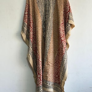 May include: A beige, red, and black patterned kaftan dress. The dress features geometric and floral designs. The kaftan is hanging on a white hanger against a white background. The dress has wide sleeves and a loose fit.