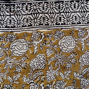 May include: A white cotton fabric with a mustard yellow floral print. The fabric features a black and white border with a repeating floral pattern.