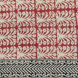 May include: A red and cream-colored textile with a repeating floral pattern. The border features a black and cream geometric design. The fabric appears to be a cotton or linen, suitable for home decor or apparel.
