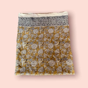 May include: A yellow fabric with a white and black floral print. The fabric has a border with a repeating pattern.