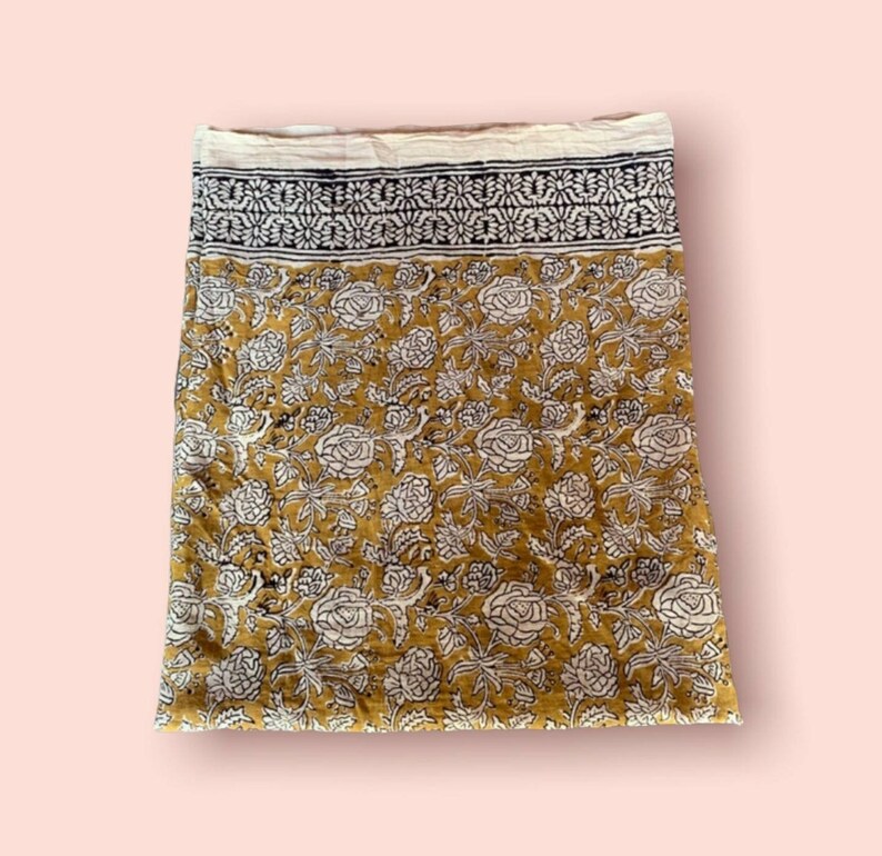 May include: A yellow fabric with a white and black floral print. The fabric has a border with a repeating pattern.