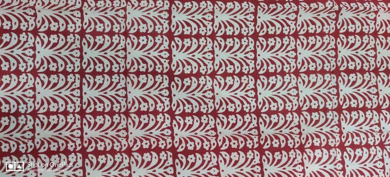 May include: A repeating pattern of white floral and leaf designs on a red background. The design is symmetrical, with each element mirroring the others. The overall effect is a decorative, textured surface.