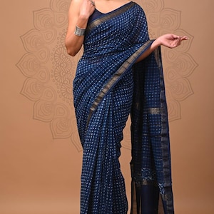 May include: A navy blue saree with a white grid pattern and gold trim. The fabric drapes elegantly, showcasing the intricate design. The saree is a traditional garment, often worn for special occasions.