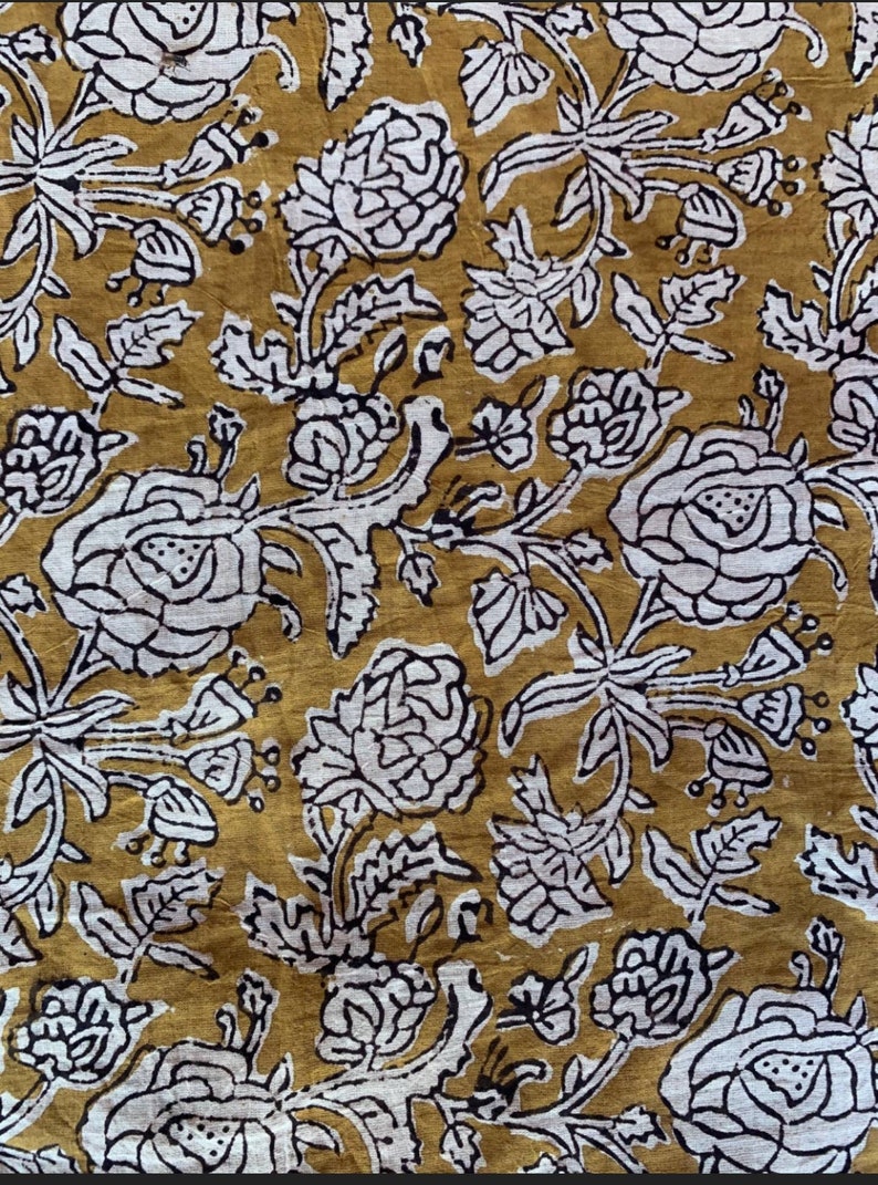 May include: A mustard yellow fabric with a white floral pattern. The flowers are stylized and have a black outline. The fabric has a vintage feel.