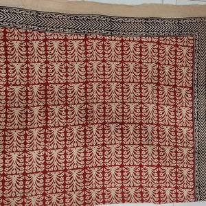 May include: A rectangular textile with a red and cream floral pattern. The design is arranged in a grid, with a black and cream border. The textile is likely a scarf or a decorative cloth.