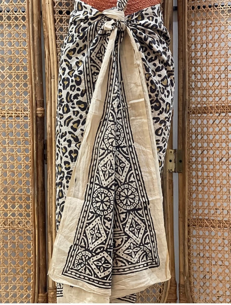 May include: A cream-colored sarong with a black and white geometric pattern. The sarong is tied around the waist and has a leopard print on the side.