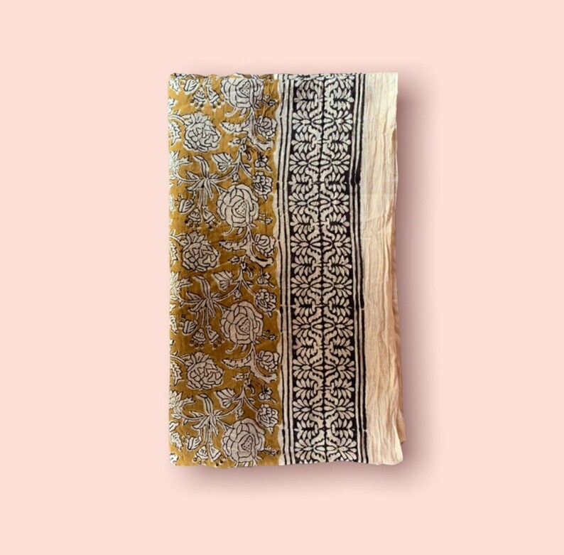 May include: A mustard yellow cotton fabric with a white floral print and black border. The fabric is folded in half and has a soft, textured feel.