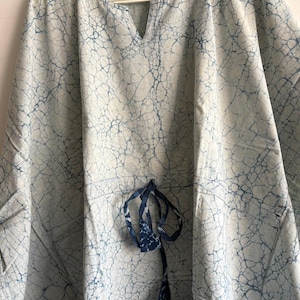 May include: A light blue and white tunic with a crackle pattern design. The tunic has a V-neck, a drawstring at the waist, and a geometric pattern at the bottom. The fabric appears to be lightweight cotton.