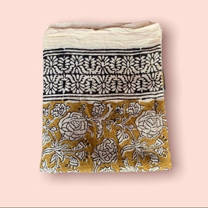 May include: A white cotton fabric with a mustard yellow and black floral print. The fabric has a border of black and white floral designs.