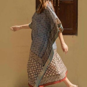 May include: A woman wearing a blue and white patterned kaftan with a geometric design. The kaftan has a long, flowing skirt and a wide, flowing sleeve. The woman is wearing a straw hat and sandals.