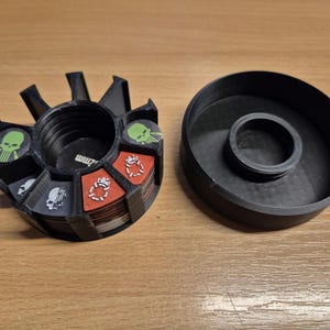 May include: A black plastic container with a rotating dial for storing and organizing small items. The container has a lid and is divided into sections. The sections are labeled with skulls and other symbols.