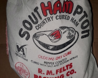 May include: A white burlap sack of country-cured ham. The bag features the words "Southampton Country Cured Ham" in a mix of red and black text. Additional text includes "Oldtime-Dry Cure" and "R.M. Felts Packing Co."