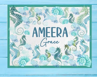 May include: A white background with a teal border, featuring a watercolor design of seahorses and seashells. The name "AMEERA Grace" is written in blue lettering.