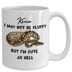 May include: White ceramic mug with a black snake illustration and the text "Kevin I may not be fluffy but I'm cute as hell"
