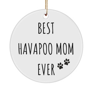 May include: A white ceramic ornament with the text "BEST HAVAPOO MOM EVER" in black. Two black paw prints are below the text. A gold string is attached for hanging.