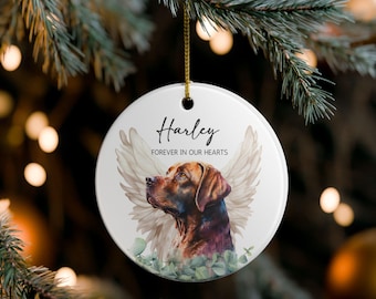 May include: A circular white ceramic Christmas decoration featuring a watercolour image of a dog with angel wings. The dog is brown and black. The name "Harley" and the phrase "Forever in Our Hearts" are printed on the ornament.