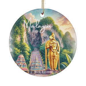May include: A round ceramic ornament with a colorful image of a temple in Malaysia. The ornament features a golden statue of a deity, lush green foliage, and the text "Malaysia 2019" and "Mark & Aimee".