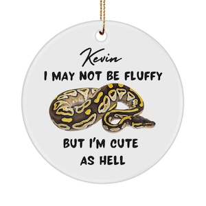 Peut inclure: Ornement de Noël en céramique blanche avec un serpent jaune et brun et le texte "Kevin I may not be fluffy but I'm cute as hell."