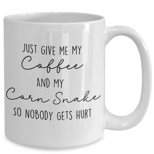 Könnte beinhalten: Weiße Keramik-Kaffeetasse mit gebogenem Henkel. Die Tasse hat einen schwarzen Text mit der Aufschrift "JUST GIVE ME MY Coffee AND MY Corn Snake SO NOBODY GETS HURT."