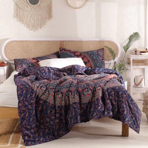 May include: A navy blue and pink paisley patterned duvet cover with a woven headboard behind it. The duvet cover has a mandala design in the centre.