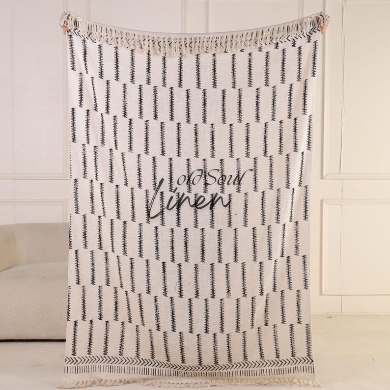 Puede incluir: Manta crema con un patr&oacute;n vertical negro repetido y flecos. Las palabras "Old Soul Linen" est&aacute;n impresas en negro. La manta est&aacute; hecha de un material suave y tejido.