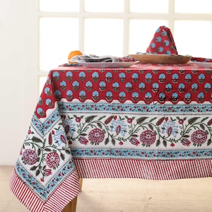 May include: A red and white floral tablecloth with a matching napkin. The tablecloth features a repeating blue floral pattern on a red background, with a white and blue floral border. The edge has red and white stripes.