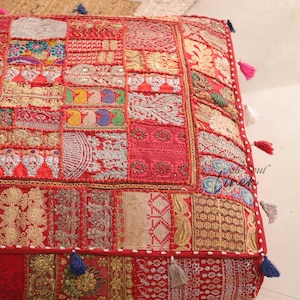 Peut inclure: Coussin de sol rouge en patchwork avec des broderies complexes et des glands. Le coussin est fait de différents tissus et présente une variété de motifs et de couleurs.