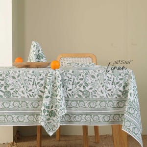 Puede incluir: Un mantel de lino blanco con un estampado floral verde y servilletas a juego. El mantel está sobre una mesa de madera, con naranjas y un cuenco de madera. El texto "old Soul Linen" es visible.